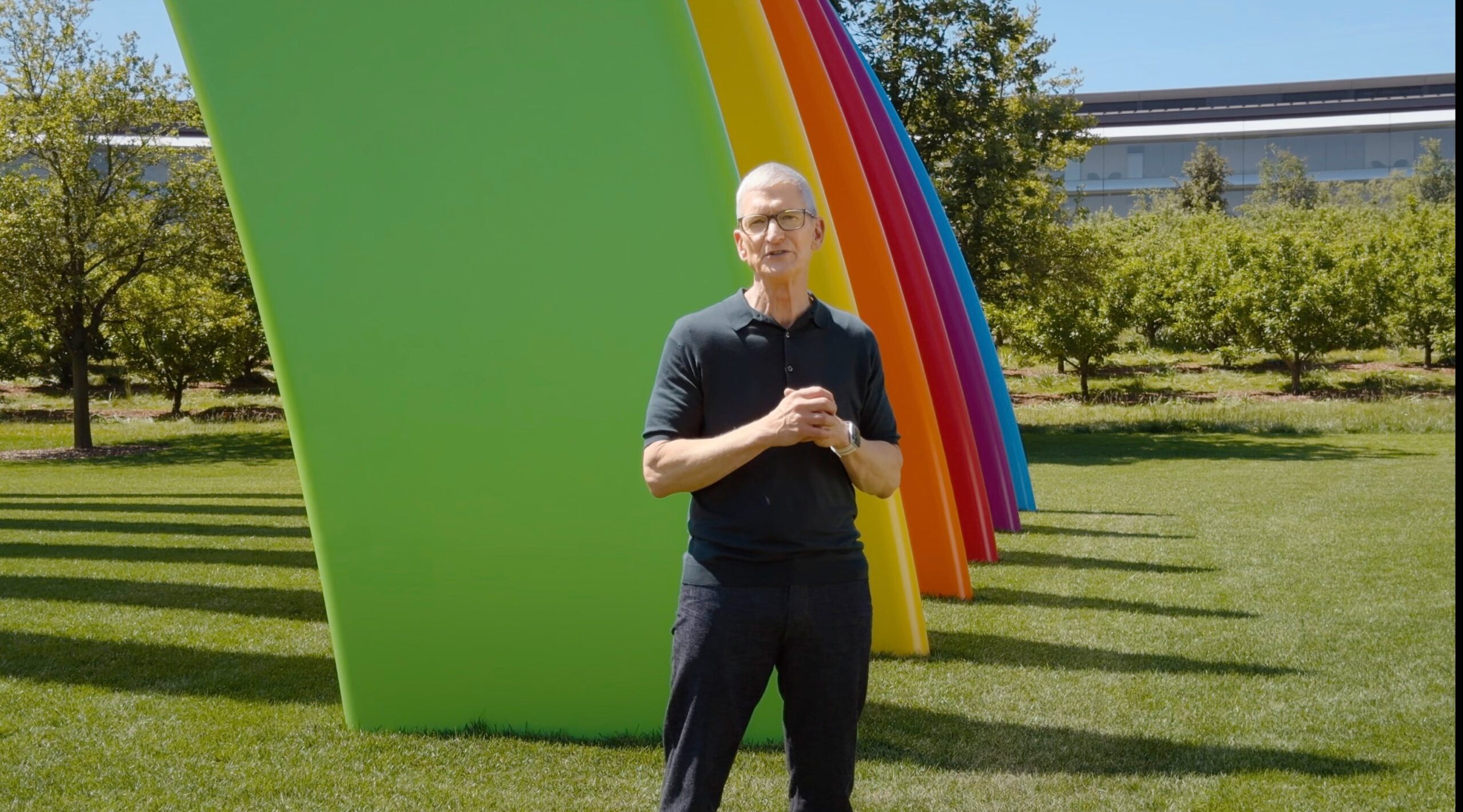 Tim Cook, in front of a plastic rainbow, which itself is in front of Apple HQ.